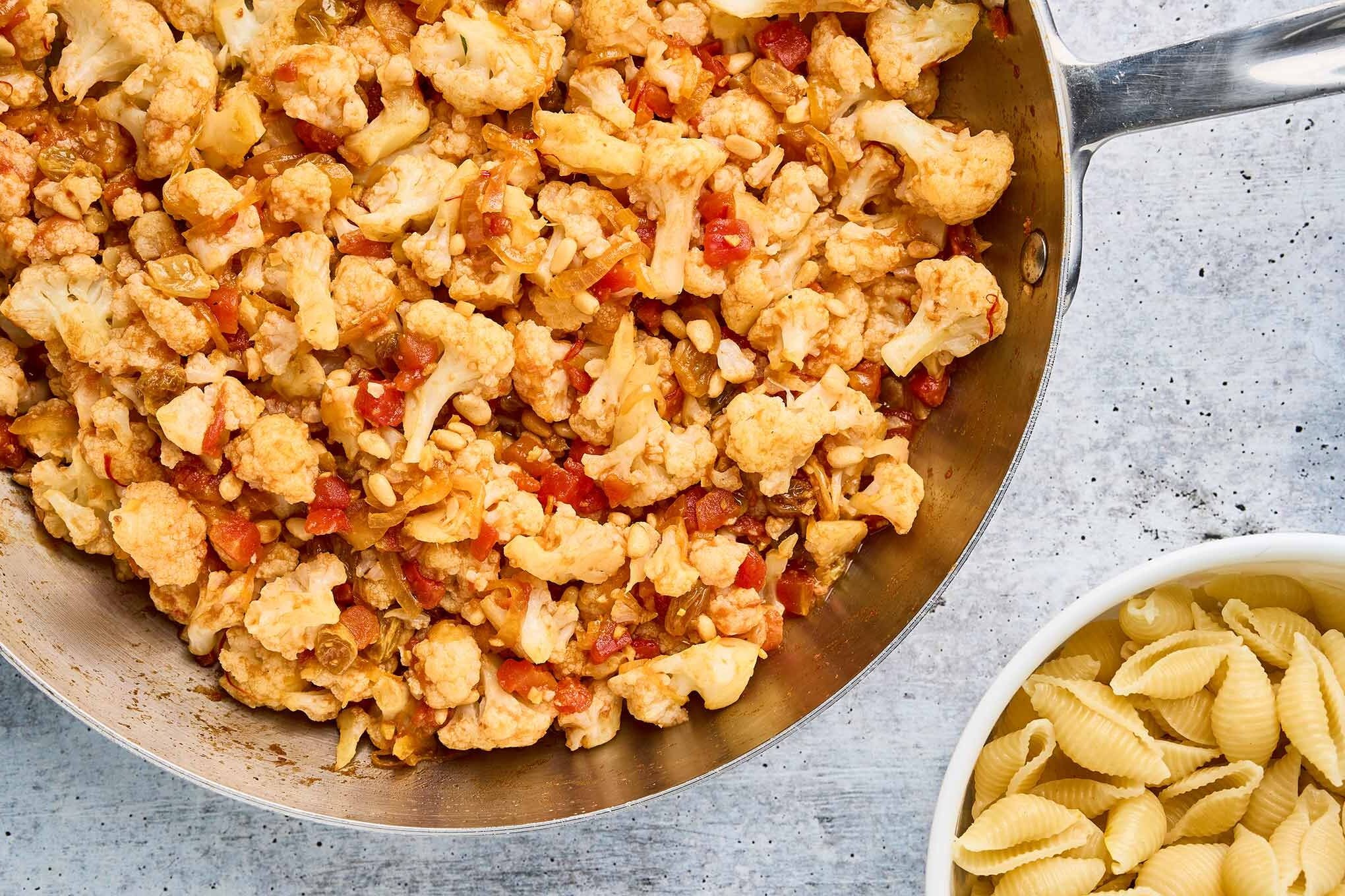 Cauliflower, tomatoes, raisins, and toasted pine nuts combined in a skillet, ready to toss with pasta for Sicilian pasta with cauliflower.