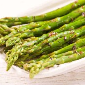 Steamed asparagus spears tossed in brown butter and balsamic vinegar on a white serving plate.