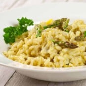 Creamy asparagus and lemon risotto garnished with parsley and asparagus tips, served in a white bowl.