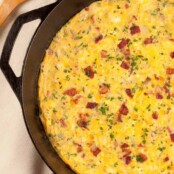 An overhead view of a bacon and cheese frittata in a cast iron pan garnished with extra bacon bits and chopped parsley.
