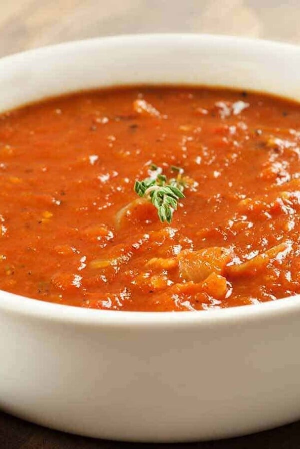 Bacon and tomato soup served in a white bowl, garnished with a small sprig of fresh thyme.