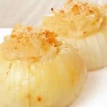 A white plate with two baked stuffed Vidalia onions filled with a creamy, sautéed onion mixture and topped with golden breadcrumbs.