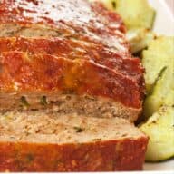 Sliced Italian turkey meatloaf on a serving platter surrounded by chunks of roasted zucchini.