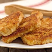Breaded, shallow-fried pork chops stacked on a serving plate with a pair of wooden serving tongs.