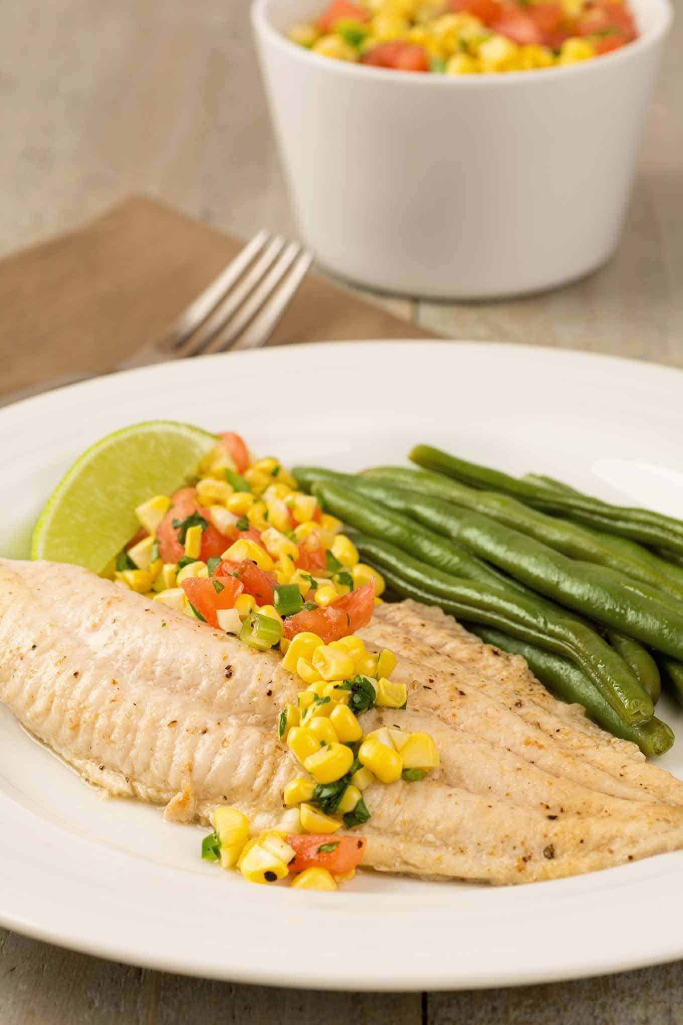 A serving of catfish and fresh corn salsa, a side of green beans, and a lime wedge.