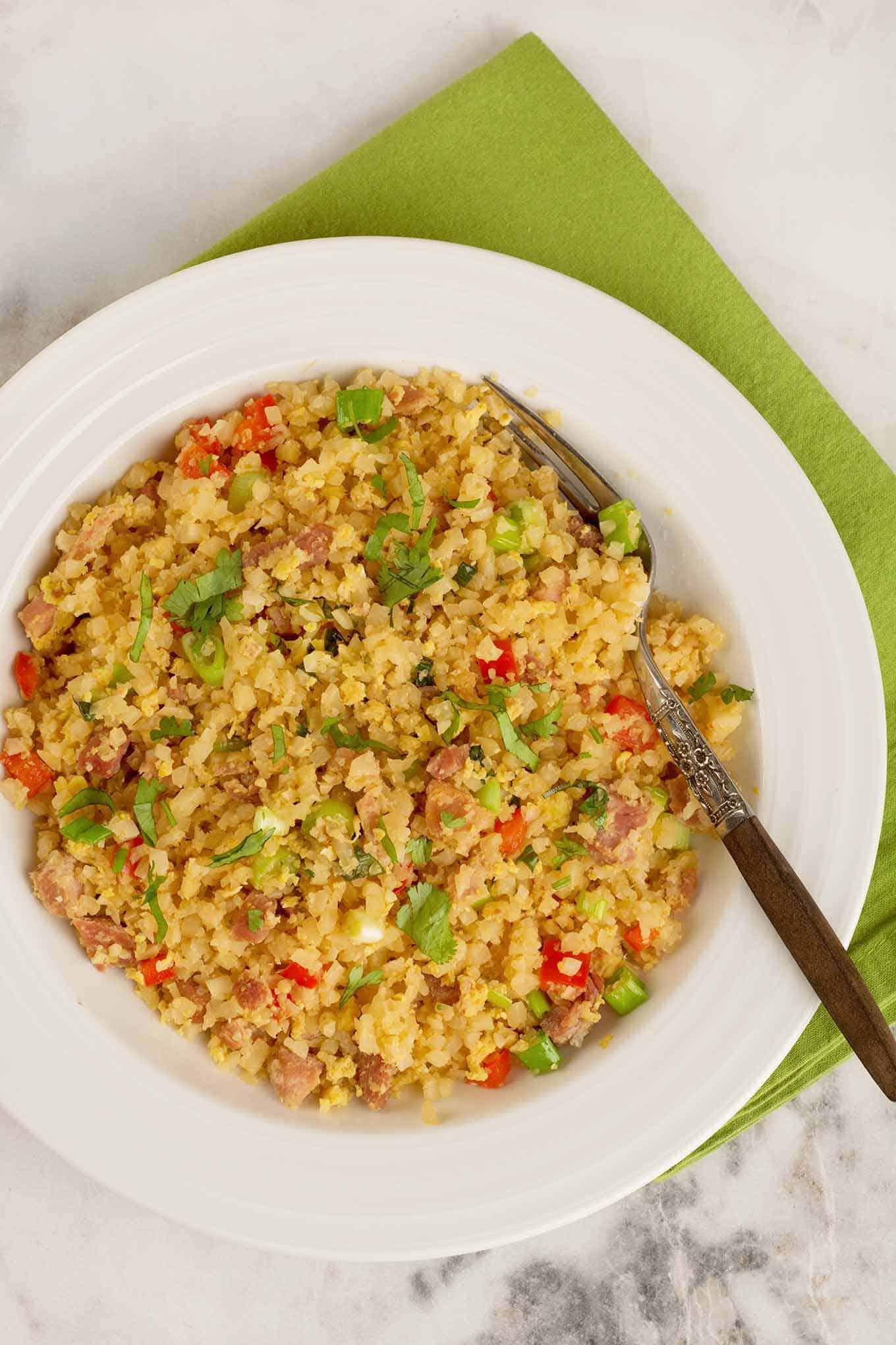 A single serving of cauliflower fried rice garnished with chopped cilantro and scallions