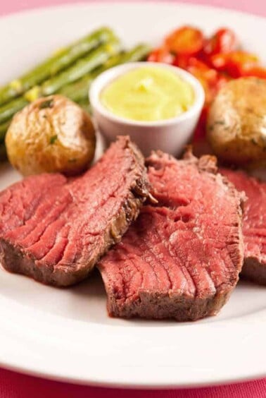 Ch&acirc;teaubriand steak served medium rare, accompanied by Sauce B&eacute;arnaise, roasted baby potatoes, roasted asparagus, and cherry tomatoes.