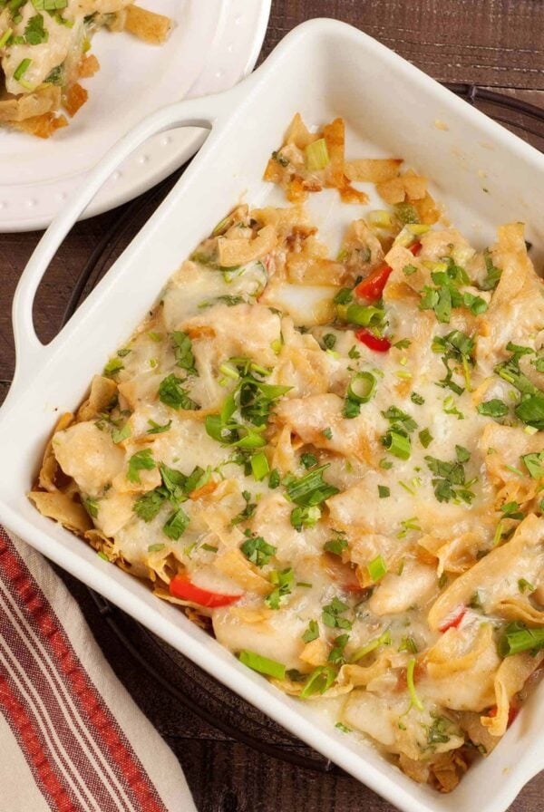 A casserole dish filled with layers of chicken in a creamy cilantro sauce, bell pepper, and pan-fried corn tortilla strips topped with mozzarella and cilantro.
