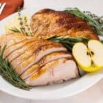 Sliced apple cider brined turkey breast on an oval serving platter garnished with a cut golden delicious apple, fresh rosemary, and fresh thyme.