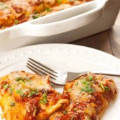 A plate of enchiladas filled with moist, tender chicken, melted cheese and cilantro and baked in a zesty homemade enchilada sauce, the casserole in the background.