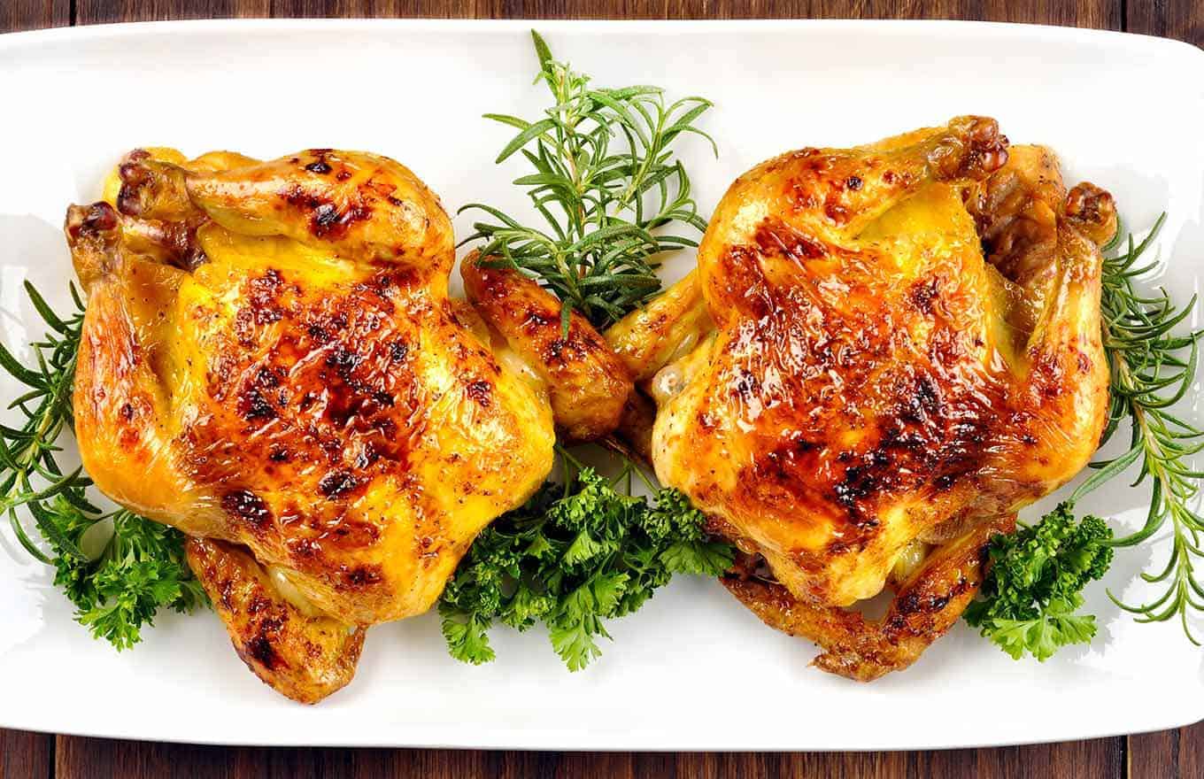 Overview of bourbon-glazed Cornish hens on a serving platter with parsley and rosemary garnish.