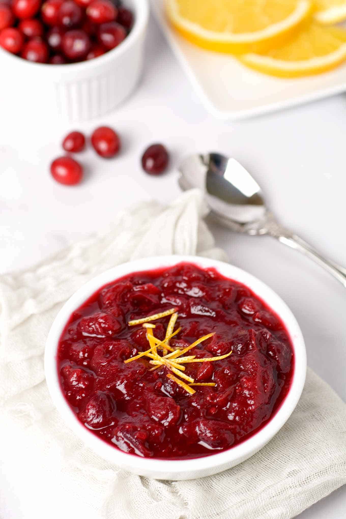 Bowl of homemade cranberry sauce with fresh cranberries and orange slices in the background.