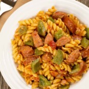 Creamy pasta with smoked sausage and green bell peppers, served in a white bowl on a rustic wood surface.