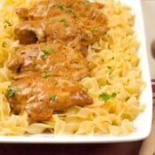 Easy Chicken Paprikas served over a bed of buttered egg noodles, garnished with chopped parsley on a rectangular white platter.