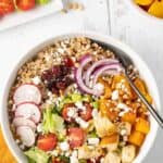 A bowl of one-dish farro salad with roasted butternut squash, dried cranberries, croutons, greens, sliced radish, and goat cheese.