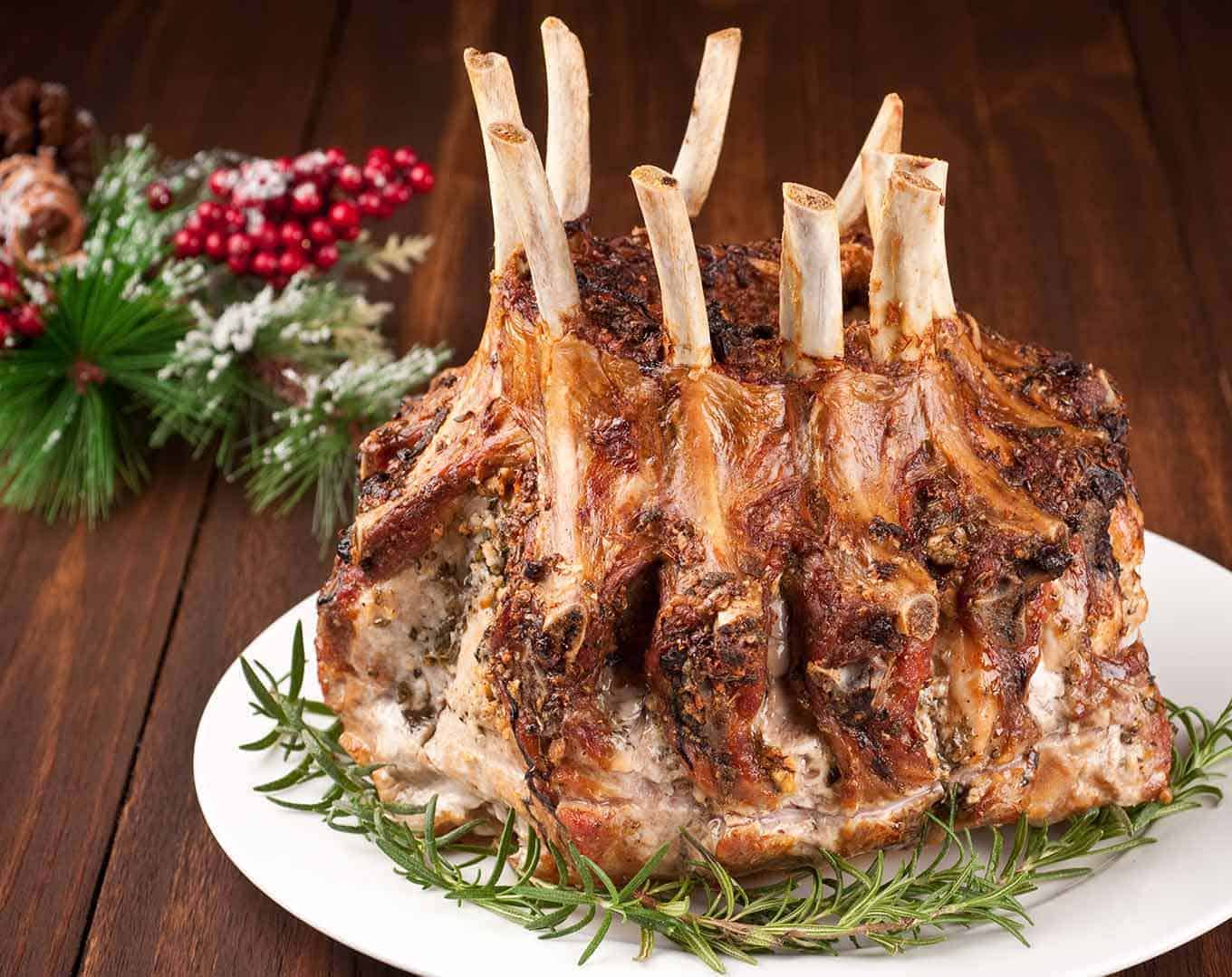 A garlic and herb crusted crown roast of pork on a round serving platter, garnished with sprigs of fresh rosemary.