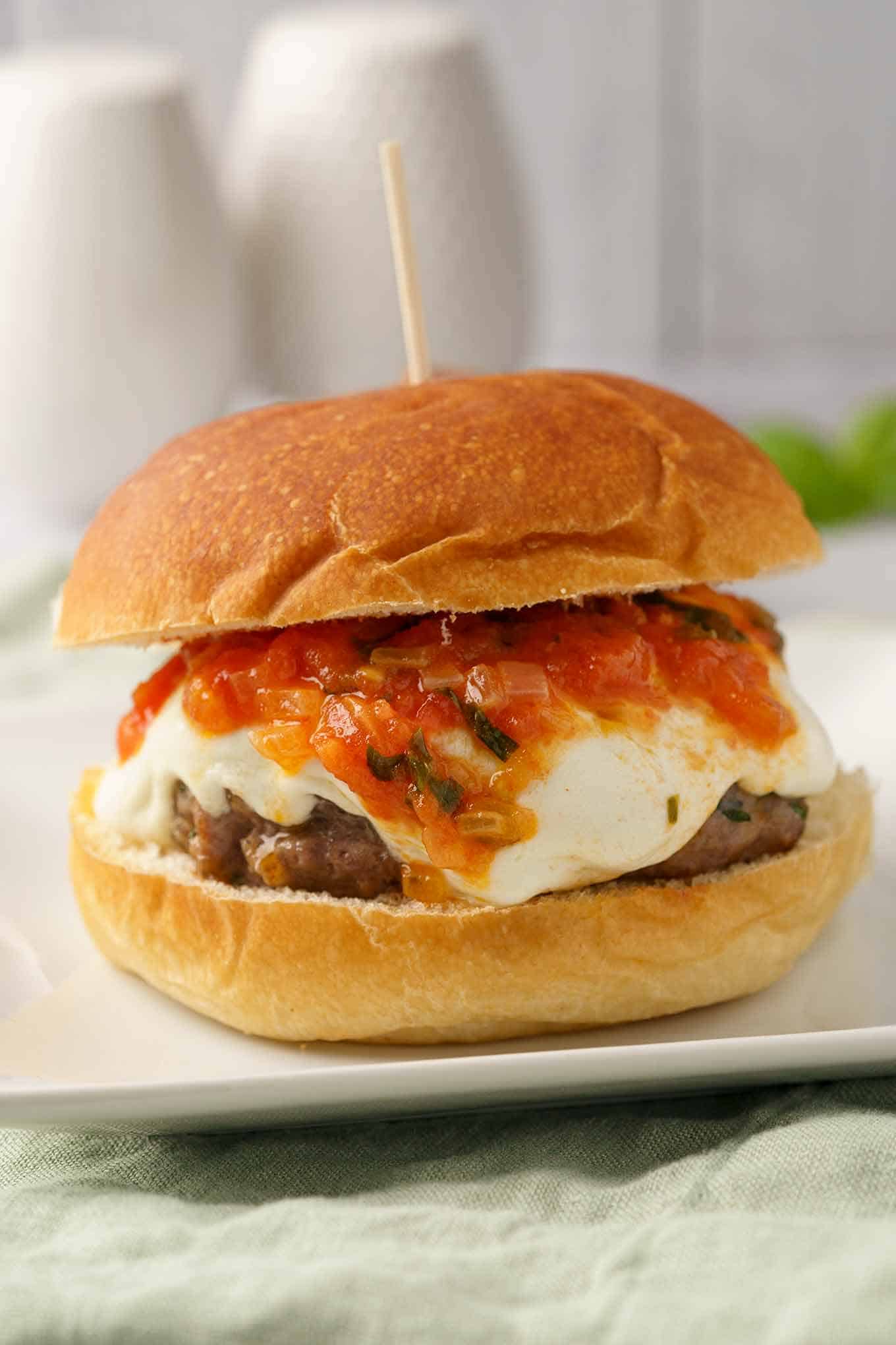 Grilled veal burger on a bun with melted mozzarella and fresh tomato sauce.