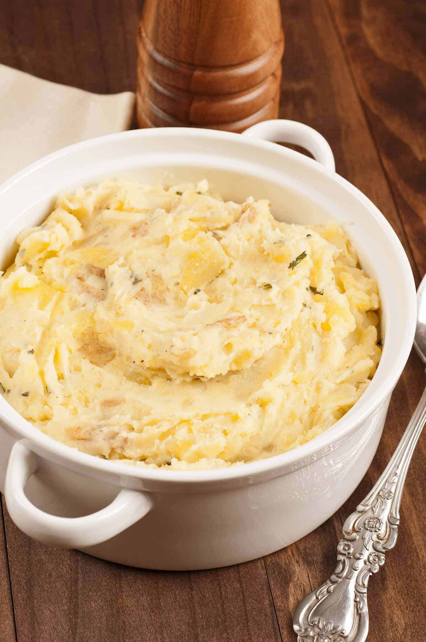 Serving bowl of rustic mashed potatoes combined with sautéed shallots, fresh thyme and sage