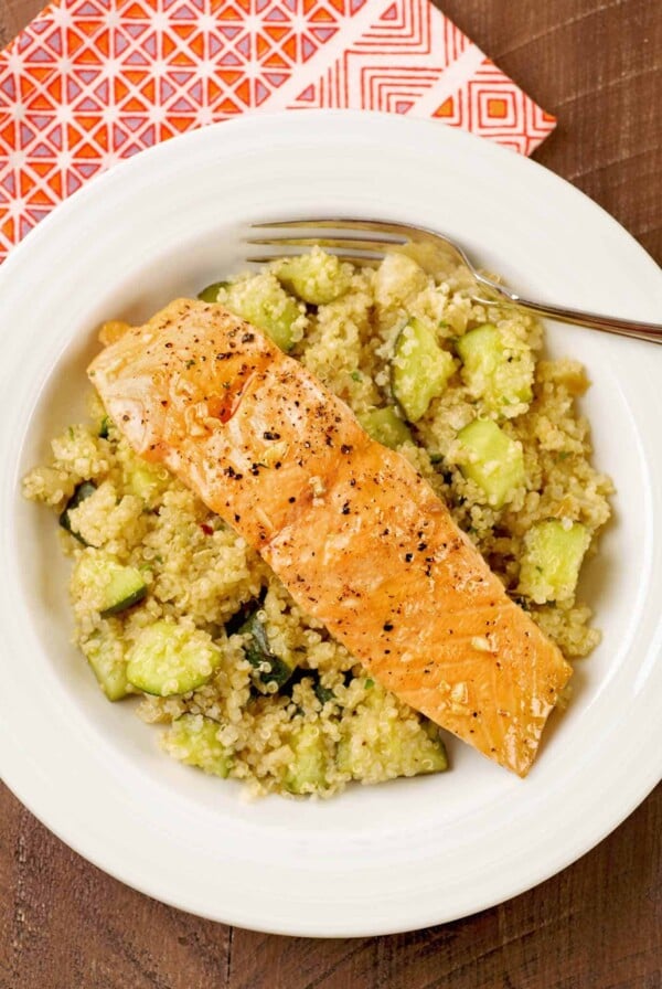 An overhead view of a bowl of quinoa combined with roasted zucchini and topped with a roasted, honey-glazed salmon fillet.