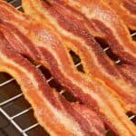Crispy strips of baked bacon lined up on a rack inside a sheet pan.