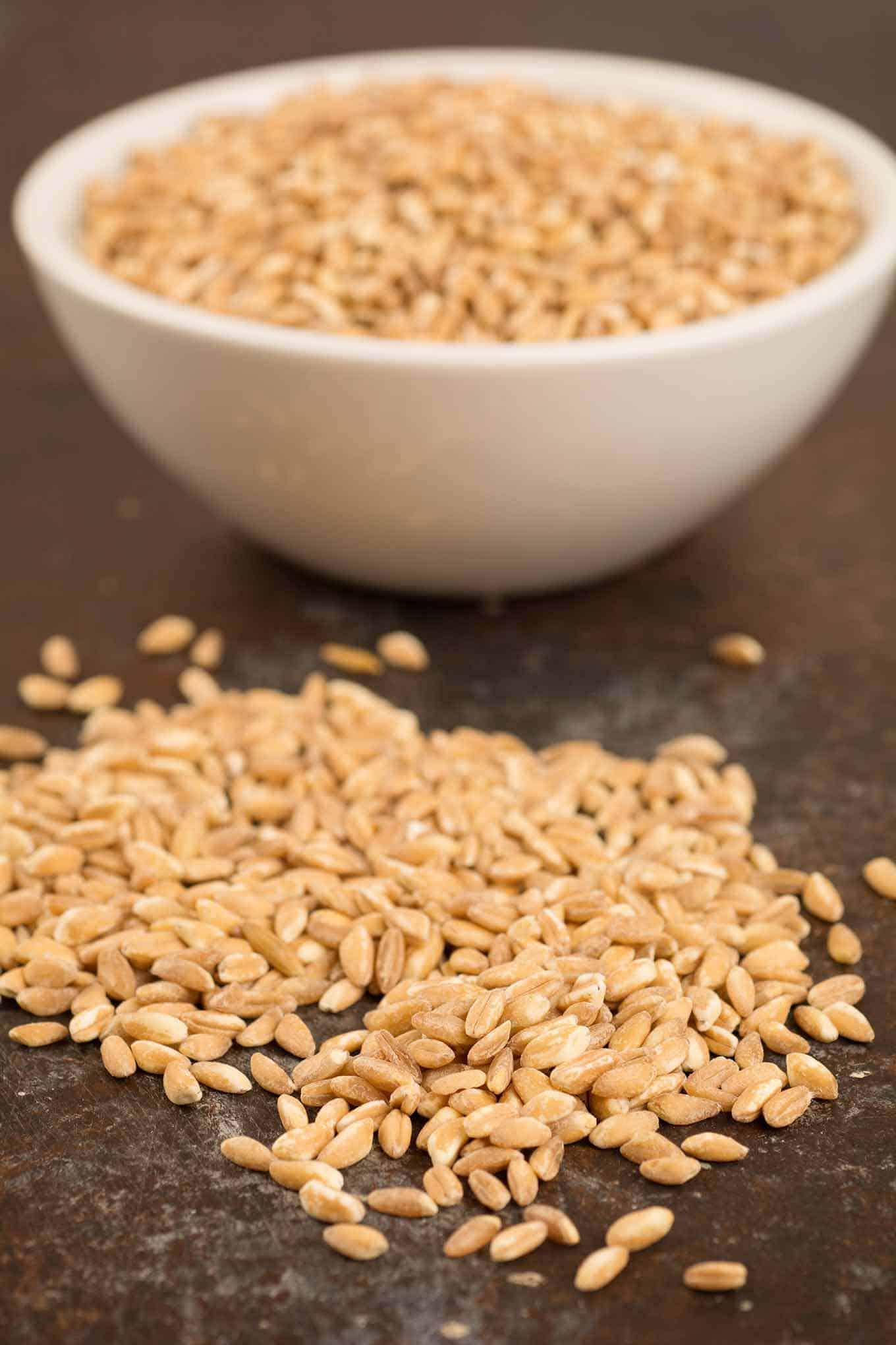 Grains of uncooked farro on the counter and in a bowl in the background