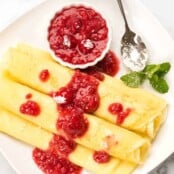 Three Hungarian crepes filled with sweetened cottage cheese, topped with raspberry sauce and powdered sugar, garnished with fresh mint.