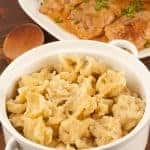 Hungarian noodle dumplings (nokedli) served in a white ceramic bowl, with a platter of creamy paprika chicken garnished with parsley in the background.