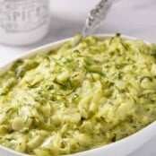 An oval serving bowl of Hungarian summer squash with dill; shredded zucchini with a flavorful sauce of sour cream, vinegar, and fresh dill.