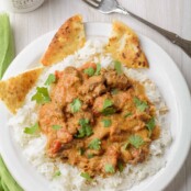 An overhead view of chunks of boneless chicken in a creamy, Indian-spiced tomato-based sauce served over rice and garnished with cilantro - pita on the side.