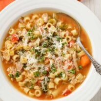 A bowl of Italian chicken soup with ditalini, carrots, escarole, and chicken, sprinkled with grated parmesan cheese and chopped fresh parsley.