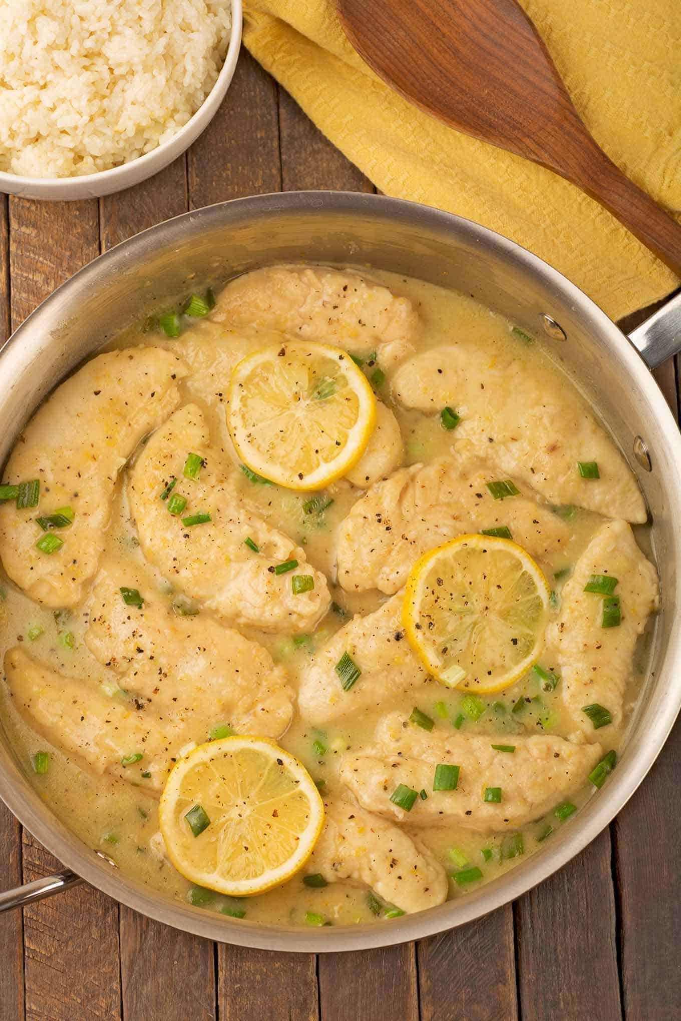 Sauté pan filled with chicken tenders in lemon pepper sauce and bowl of rice on the side