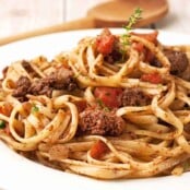 A plate of linguine topped with chicken liver ragu, featuring chunks of chicken liver, diced tomatoes, and fresh thyme.