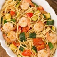 An overhead view of an oval casserole filled with sautéed zucchini and red bell pepper tossed in a light garlic sauce with linguine and shrimp.