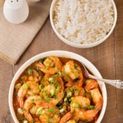 An overhead view of a bowl of Louisiana style shrimp stew in gravy with a bowl of steamed white rice and salt and pepper shakers to the rear and side.