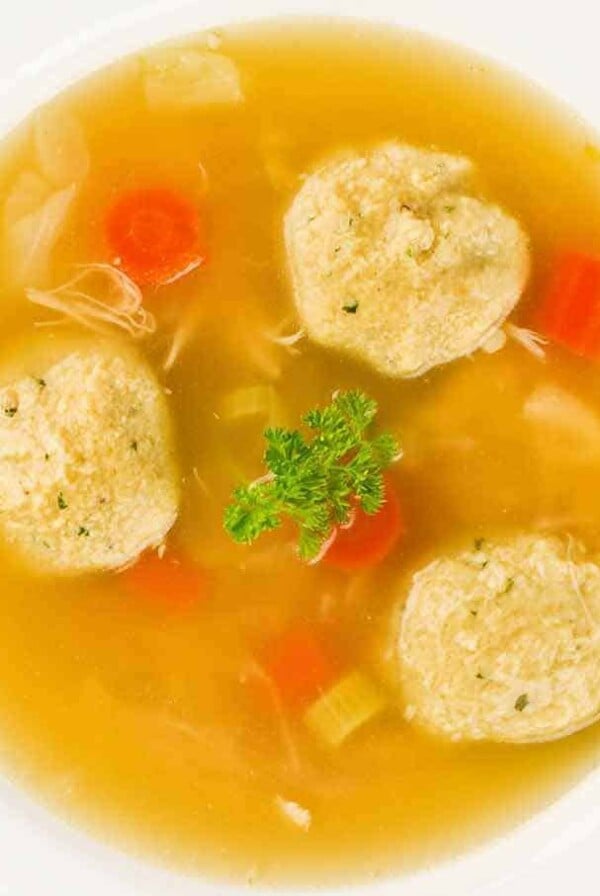 Overhead view of a bowl of matzo ball soup with carrots, celery, shredded chicken, and parsley in clear broth.