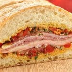 Close-up of a Mediterranean Muffuletta sandwich layered with cured meats, cheese, and olive tapenade on crusty ciabatta bread.
