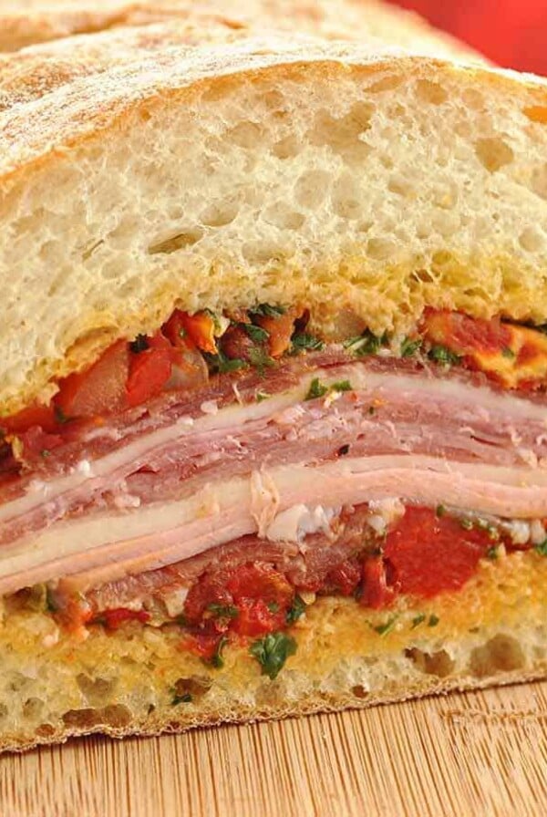 Close-up of a Mediterranean Muffuletta sandwich layered with cured meats, cheese, and olive tapenade on crusty ciabatta bread.