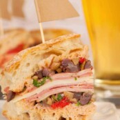 A close view of a cut muffaletta sandwich stacked with layers of deli meats, cheese, and olive salad on crusty bread.
