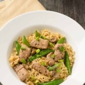 A shallow bowl of ramen noodles tossed with stir-fried pork, sugar snap peas, and scallions in soy-ginger sauce.