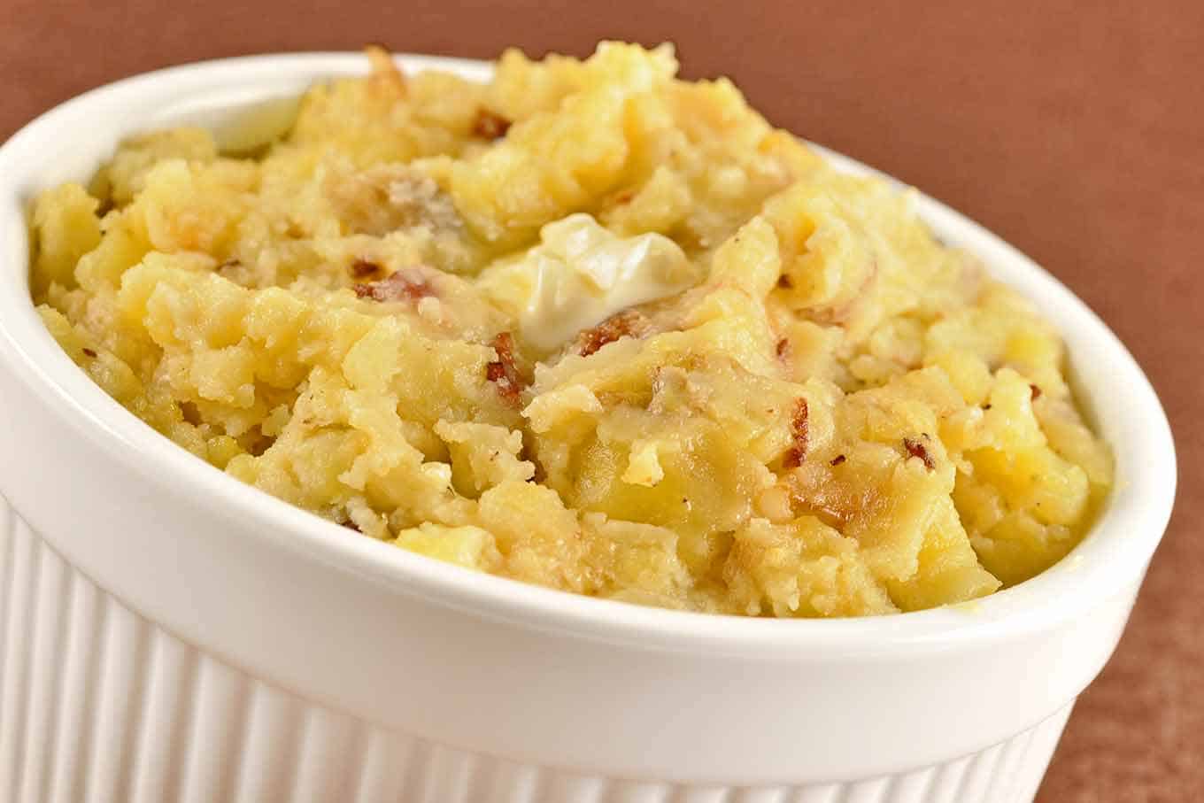 Serving bowl of rustic smashed potatoes with bacon bits and sautéed onion