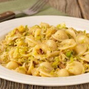 A plate orecchiette pasta tossed with sautéed shredded Brussels sprouts and bacon, a fork and napkin in the background.