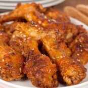Crispy oven-fried chicken wing drumettes coated in a golden glaze and sprinkled with sesame seeds, served on a white plate.
