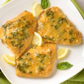 Three pieces of breaded, oven-fried fish fillets topped with lemon butter infused with fresh basil and garnished with basil leaves and lemon wedges.