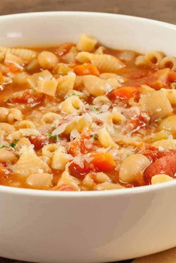 A close-up of a white bowl filled with pasta e fagioli soup, showing pasta, beans, and vegetables in a broth.