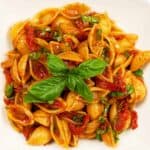 Serving dish filled with shell pasta tossed with sun-dried tomatoes, balsamic glaze, and fresh basil.