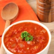 Bowl of chunky tomato sauce with diced onions and orange peel, garnished with fresh parsley.