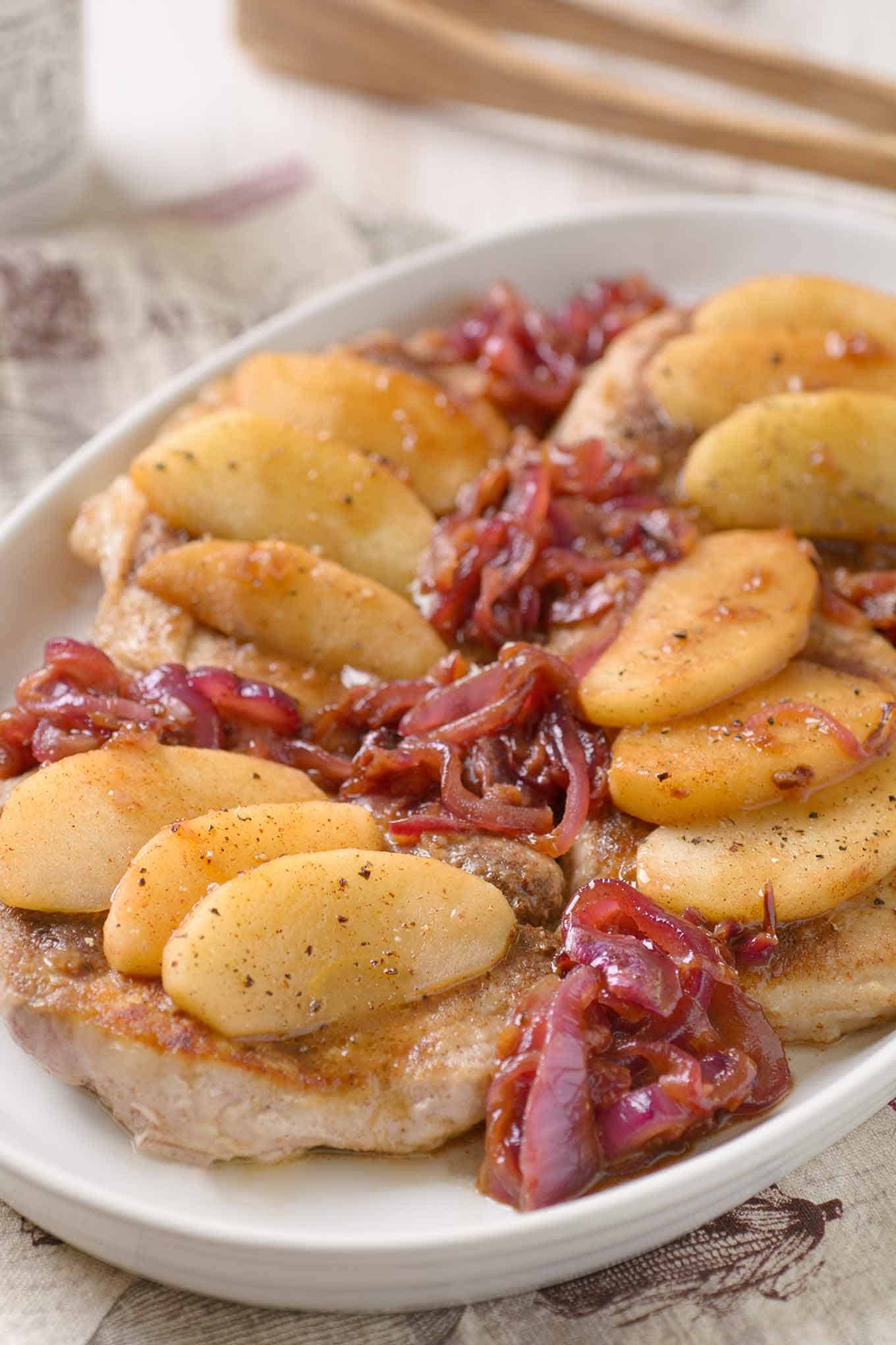 Boneless pork chop topped with three apple slices and cider pan sauce with caramelized red onions on the side.