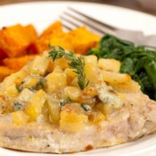 A plate with a boneless pork chop, pan-seared and topped with sautéed chopped pears, blue cheese, and thyme with side dishes of sweet potatoes and spinach.