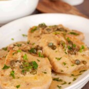 Pork scallopine with dijon-caper cream sauce, garnished with chopped parsley and served on a white plate.