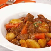 Bowl of pressure cooker beef stew with tender chunks of beef, potatoes, carrots, and rich brown gravy, garnished with thyme.